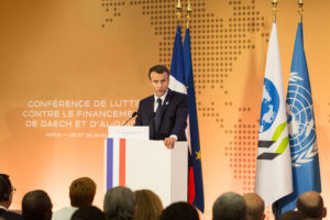 Emmanuel Macron sur une estrade, appuyé à un pupitre, devant un auditoire.