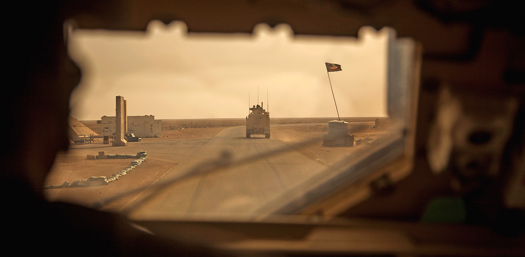 photo prise de l'intérieur d'un char américain en Irak. Un blindé avance dans une route au milieu du désert