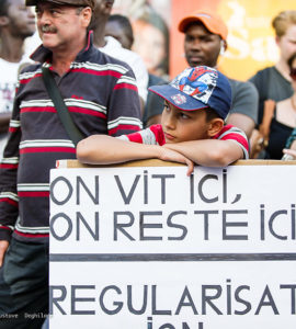 Enfant avec un panneaux qui dit "I vit, ici, on reste ici" pendant Manifestation pour le droit des migrant-e-s