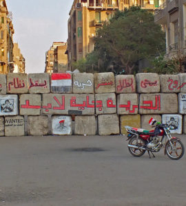 barricade au caire avec des blocs de bêton avec des graffitis dessus et une moto devant avec le drapeau égyptien