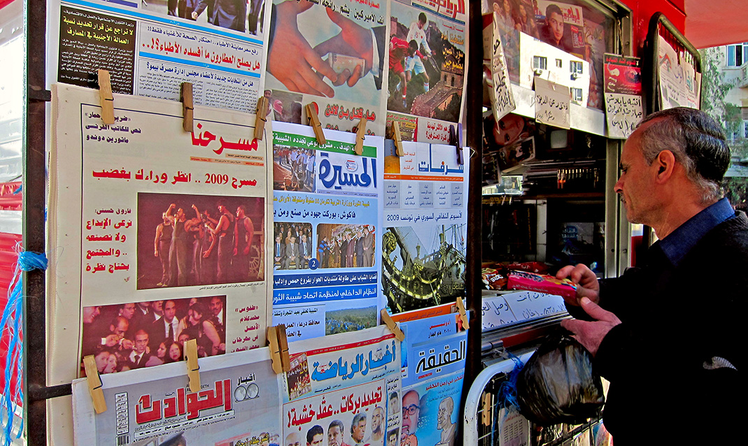 kioske dans un pays arabe avec les journaux affichés et un homme qui achète une copie
