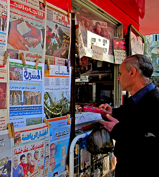 kioske dans un pays arabe avec les journaux affichés et un homme qui achète une copie