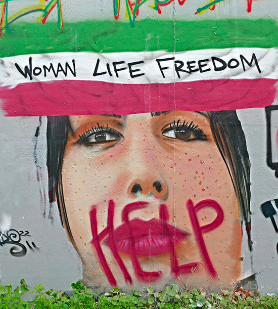 graffiti représentant un portrait de femme iranienne. Au-dessus d'elle, un drapeau iranien avec le texte "Woman life freedom". Sur sa bouche le texte "Help"