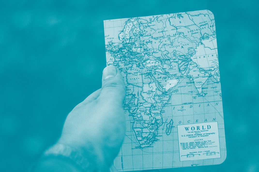 Une main tient un cahier avec la carte du monde sur la couverture