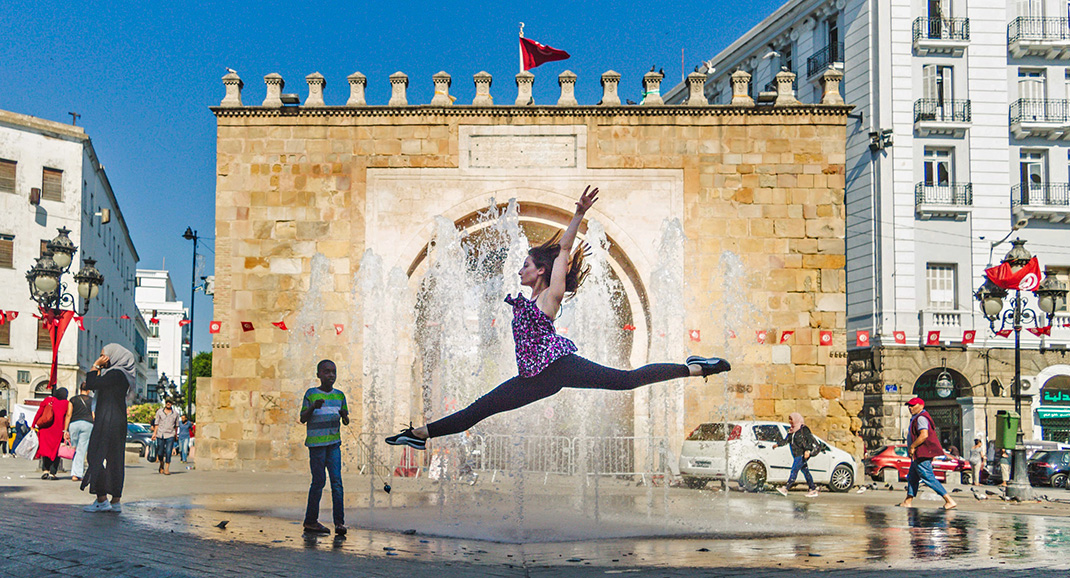 Une danceuse saute devant une fontaine à Bab Bhar à Tunis. Derrière elle, un garçon la regarde avec curiosité