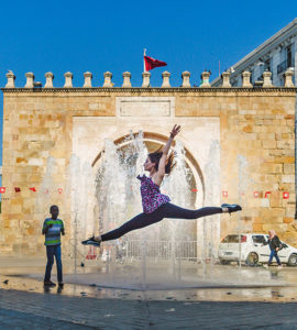Une danceuse saute devant une fontaine à Bab Bhar à Tunis. Derrière elle, un garçon la regarde avec curiosité