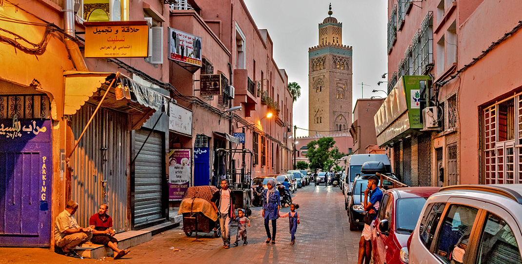 Personnes dans une rue de Marrakech au coucher du soleil avec un minaret sur le fond