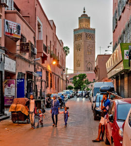 Personnes dans une rue de Marrakech au coucher du soleil avec un minaret sur le fond