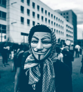 Un manifestant avec le masque du personnage de "V pour Vendetta" et un keffieh autour de sa tête