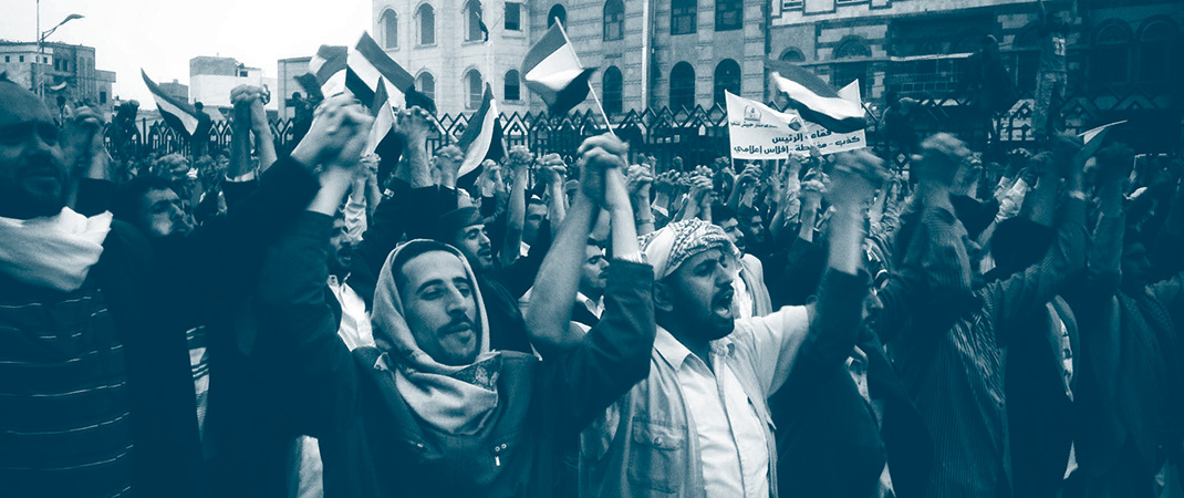 Manifestants dans les rues de Sanaa au Yémen se tiennent la main et chantent l'hymne national entourés par des drapeaux du Yémen