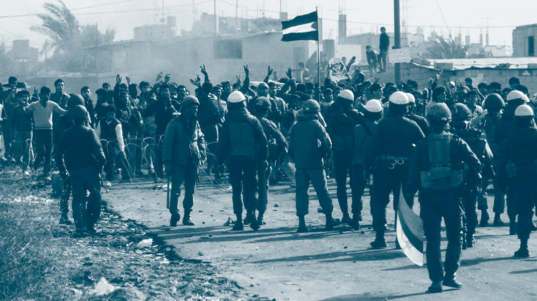 Un groupe de manifestants brandissant un drapeau palestinien à Gaza pendant la 1er intifada devant les troupes antiémeute israélienne