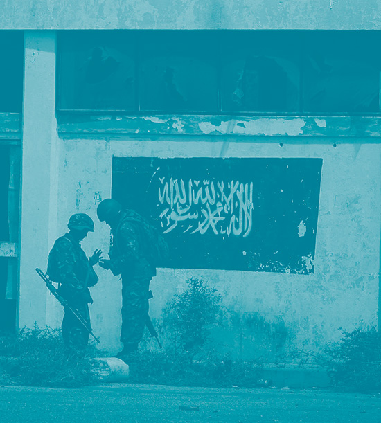 Deux soldats parlent entre eux devant le drapeau du groupe islamiste Al Shabaab, affilié d'Al-Qaeda, dessiné sur un mur