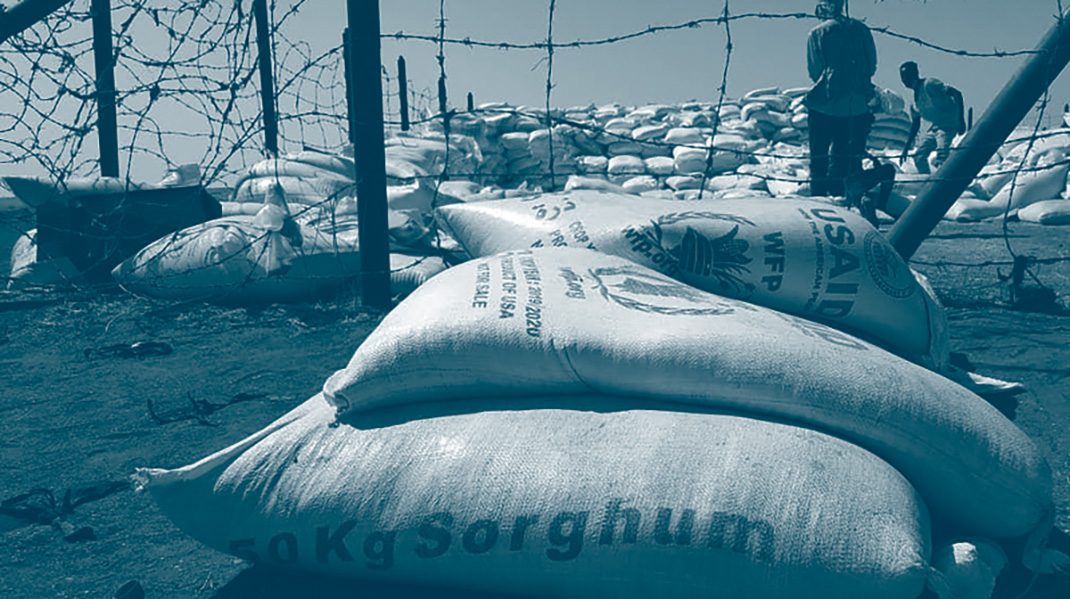 des sacs de sorghum devant un barbelé au Sudan pour une distribution d'aide humanitaire
