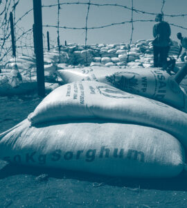 des sacs de sorghum devant un barbelé au Sudan pour une distribution d'aide humanitaire