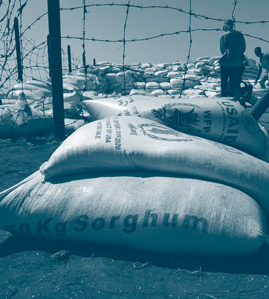 des sacs de sorghum devant un barbelé au Sudan pour une distribution d'aide humanitaire