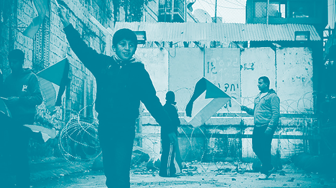 En enfant brandit un drapeau palestinien à Hébron devant un mur de séparation. Avec lui sur le fond d'autres personnes, elles aussi avec un drapeau de la Palestine