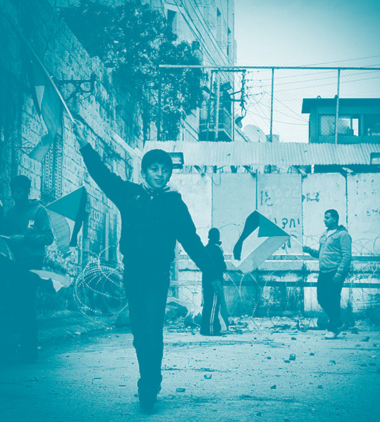 En enfant brandit un drapeau palestinien à Hébron devant un mur de séparation. Avec lui sur le fond d'autres personnes, elles aussi avec un drapeau de la Palestine