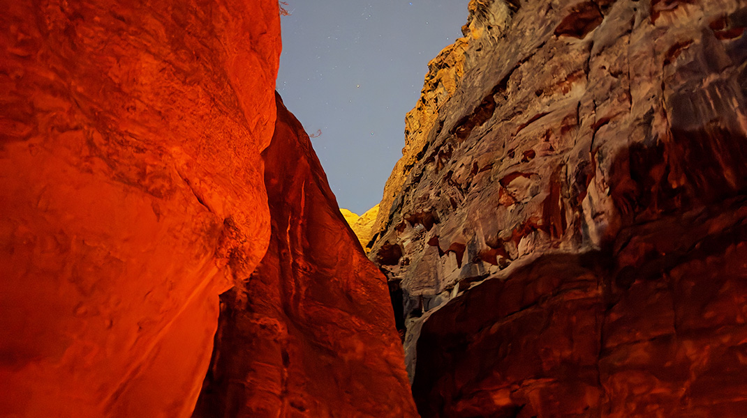 nuit qui avance sur les roches de Pétra en Jordanie. Une roche rouge sur la gauche devant une roche jaune sur la droite et le ciel étoilé sur elles