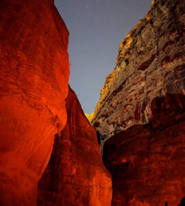 nuit qui avance sur les roches de Pétra en Jordanie. Une roche rouge sur la gauche devant une roche jaune sur la droite et le ciel étoilé sur elles