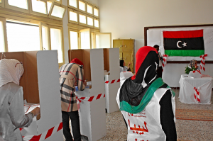 Dans un bureau de vote en Libye une femme de dos avec un voile avec les couleurs du drapeau libyen contrôle les opérations de vote de deux autres femmes